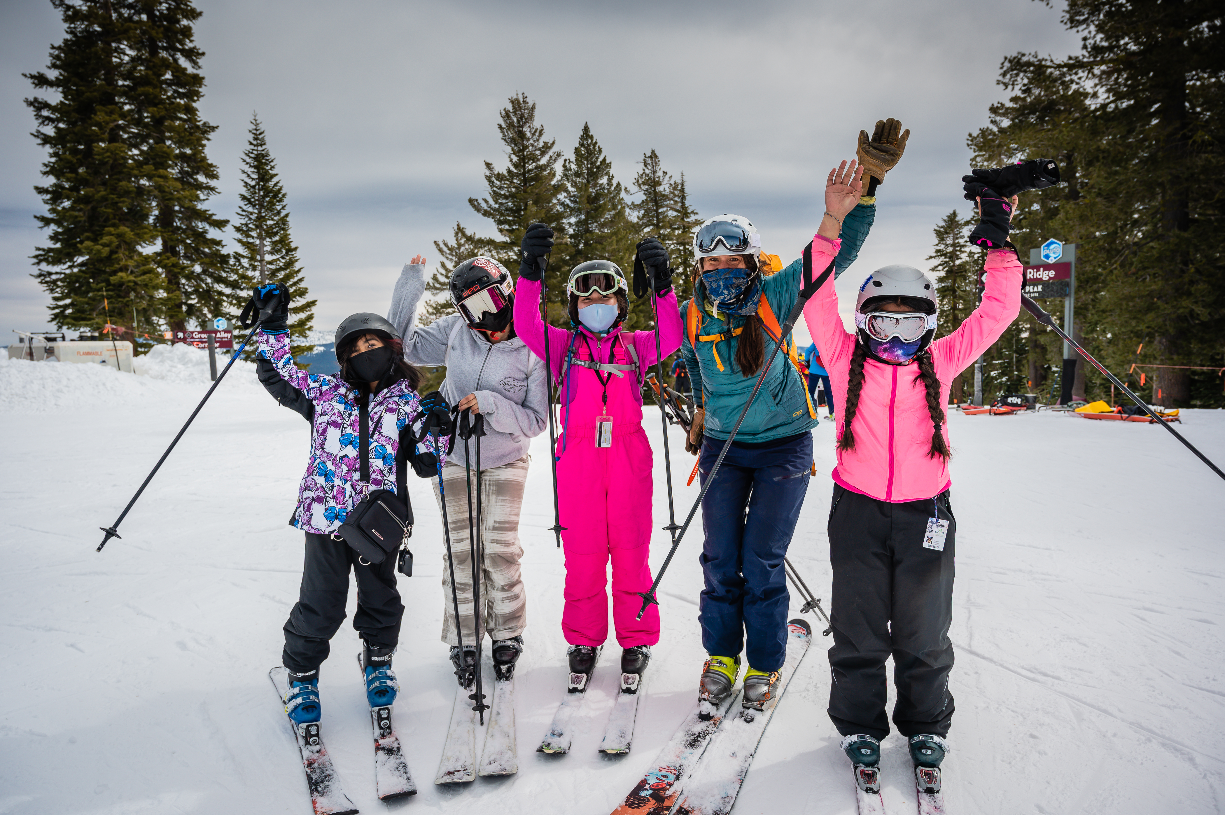 several kids stand with an adult mentor while wearing skis and raising their arms